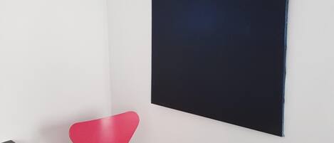 Une pièce avec une chaise rouge, une œuvre d’art noire accrochée au mur et un plancher en bois.