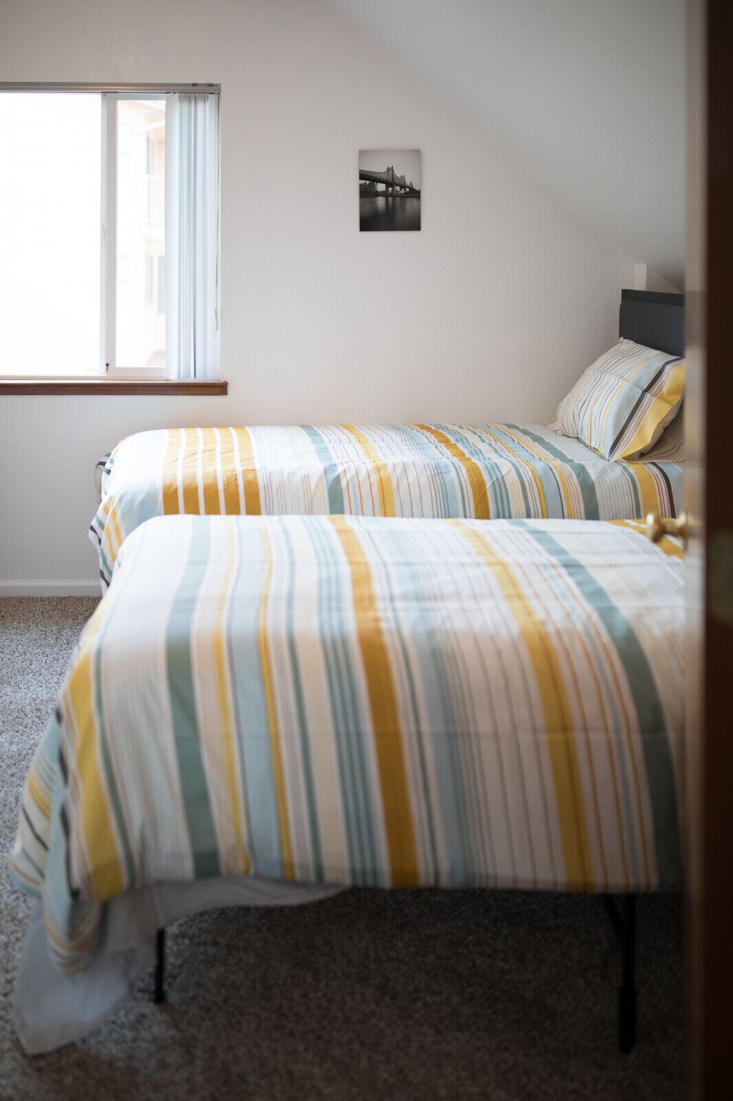 A bedroom with two beds, a window with curtains, and a wall-mounted picture.