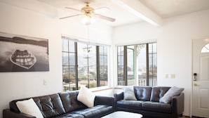 A spacious living room with two leather sofas, a coffee table, and large windows offering a view of a lake and mountains. - Large House on a Hill- 15 Min Walk 2 Bart (Richmond)