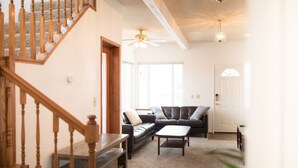 Ein Wohnzimmer mit Treppe, einer Ledersofa, einem Couchtisch und einem Deckenventilator.