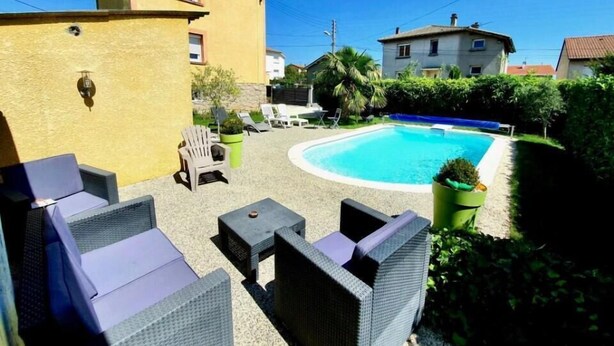 Zona de piscina con mobiliario exterior y un edificio amarillo.