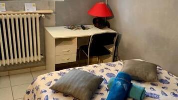 Un dormitorio con una cama, un escritorio, una silla, una lámpara roja y un televisor en la pared.