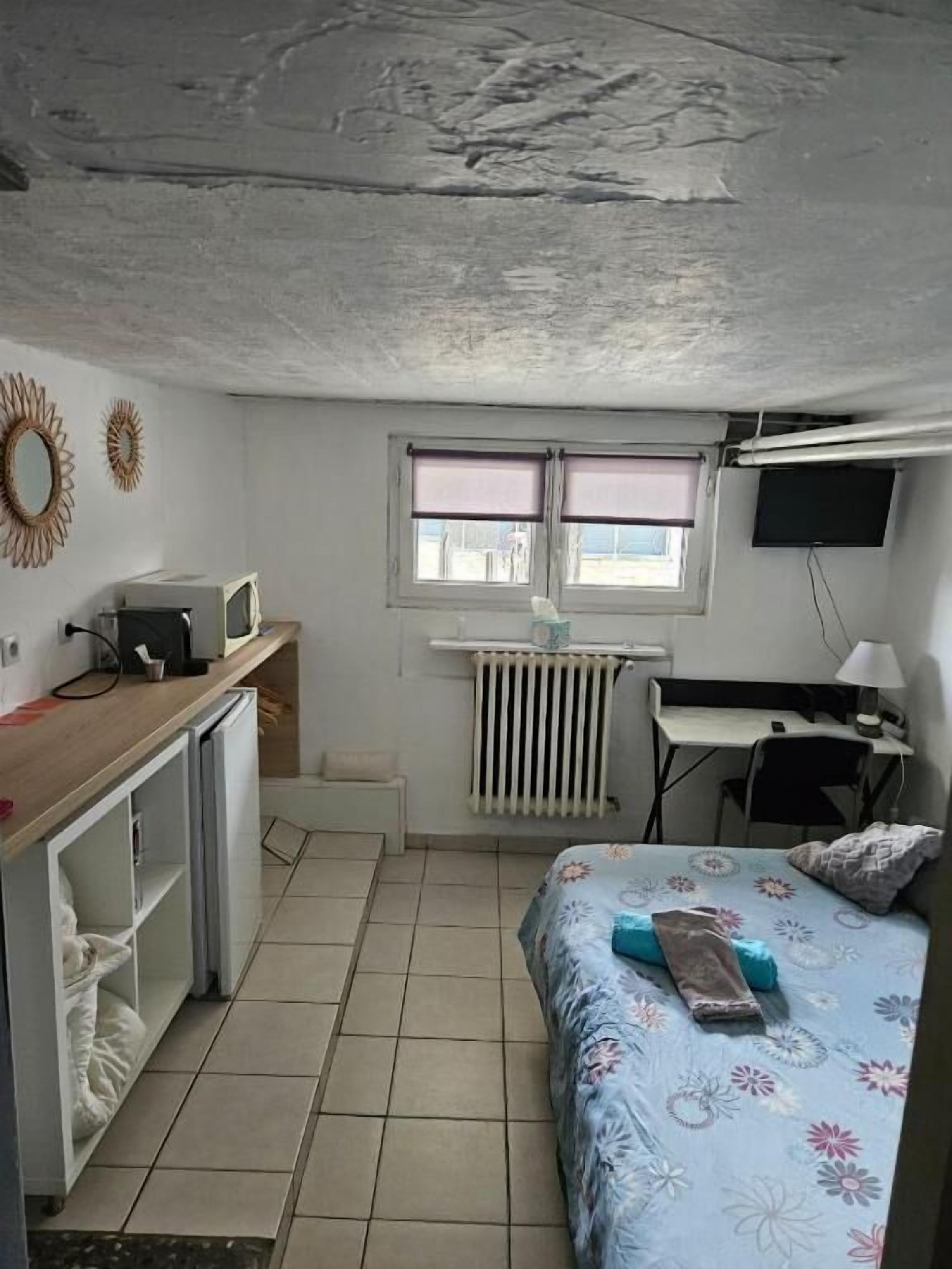 Une petite pièce comprenant un lit, un bureau, un radiateur, une télévision et une fenêtre.