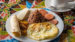 A plate of breakfast food including eggs, sausage, and plantains on a colorful tablecloth. - Hotel FAS & OFF Site Thermal Resort (La Fortuna)