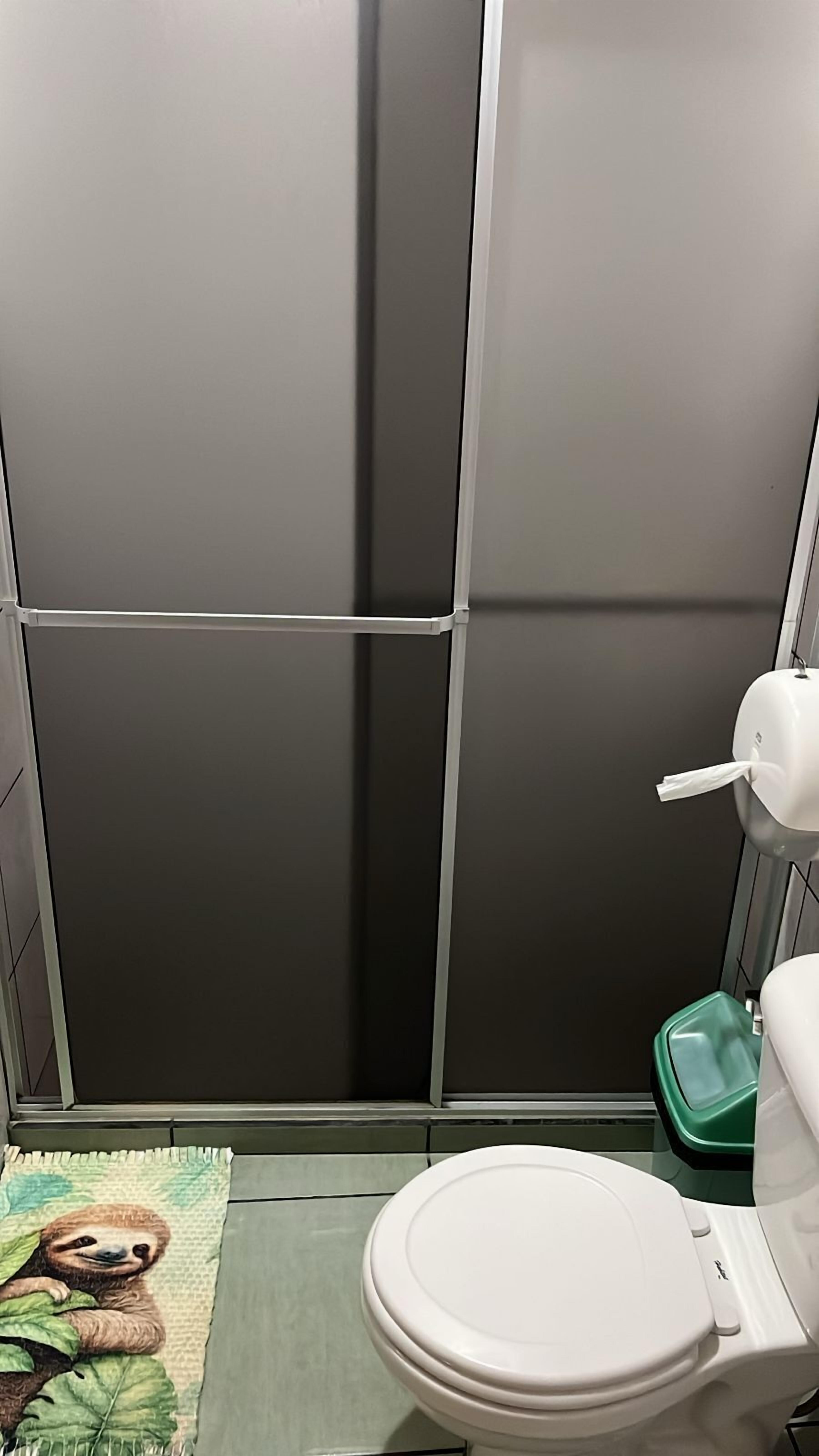 A bathroom with a toilet, a green trash bin, and a shower area.