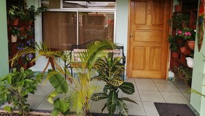 A house with a tiled porch, a sliding glass door, and a wooden door. There are potted plants on both sides of the porch. - Hotel FAS & OFF Site Thermal Resort (La Fortuna)