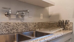 A kitchen with two stainless steel sinks, a granite countertop, and a wire rack holding utensils. - Spotless Back House (Fresno)