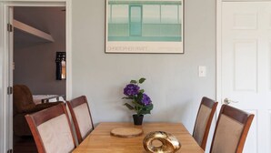 A dining room with a wooden table, four chairs, a vase with purple flowers, and a framed artwork on the wall. - Spotless Back House (Fresno)
