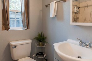 Une salle de bain avec des toilettes, un lavabo et une fenêtre avec des rideaux.