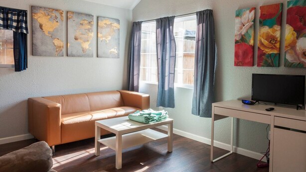 A living room with a sofa, a coffee table, a TV on a desk, and artwork on the walls. - Spotless Back House (Fresno)