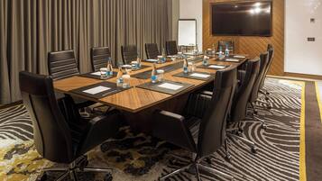 A conference room with a long table, multiple chairs, water bottles, and a large screen on the wall.