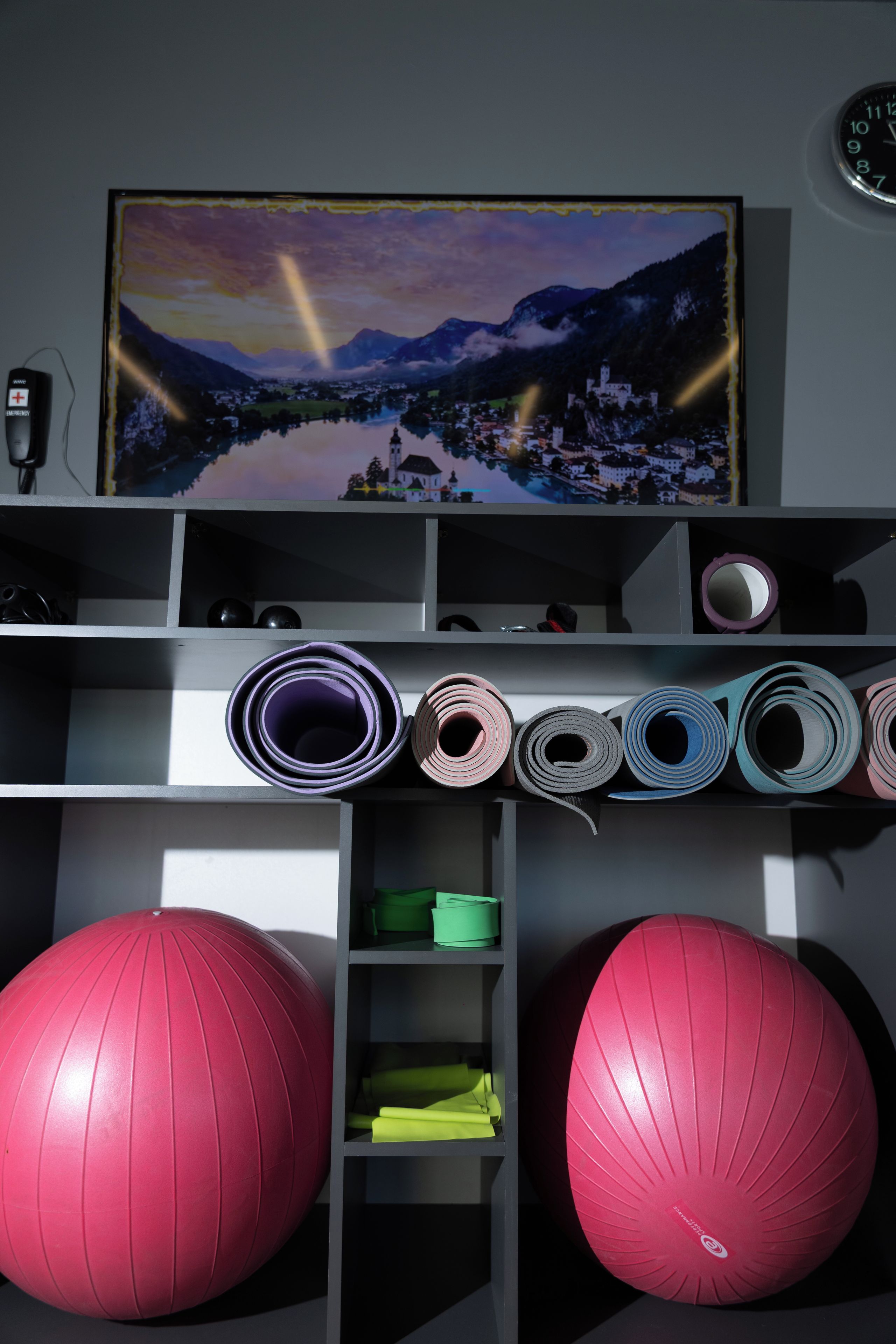 A room with a television displaying a scenic landscape, exercise balls, and a clock on the wall.