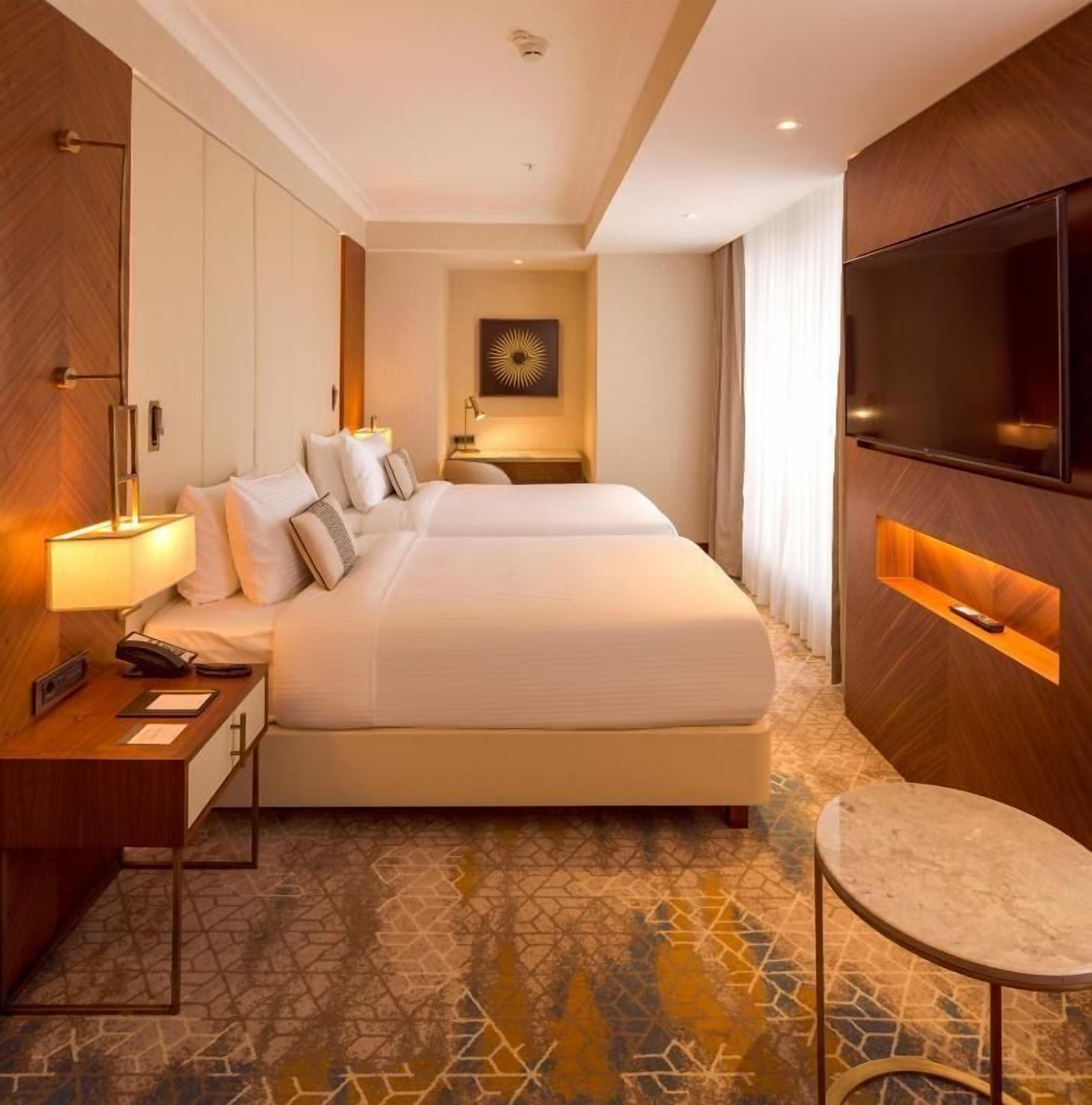 A hotel room with a large bed, bedside tables, a TV, and a patterned floor.
