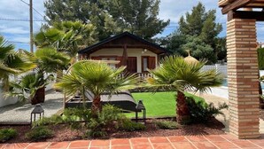 A small house with a wooden exterior, surrounded by a garden with palm trees and a lawn.