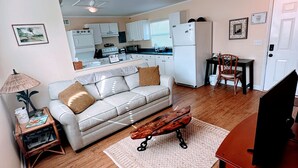A compact living space with a sofa, coffee table, and a dining area with a chair. A kitchen is visible in the background with white cabinets and appliances. - Perfect for two on the River at Mel Fishers Museum  (Sebastian)
