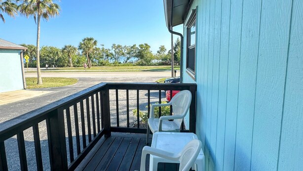A covered porch with two white plastic chairs, a wooden railing, and a view of a road with palm trees and a building in the distance. - Perfect for two on the River at Mel Fishers Museum  (Sebastian)