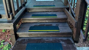 A wooden front door with a keypad lock, a welcome mat, and a set of wooden steps with yellow tactile strips. - Perfect for two on the River at Mel Fishers Museum  (Sebastian)
