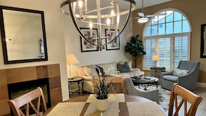 A spacious living room with a fireplace, a dining area with a table and chairs, a large chandelier, and a view of the outside through a window. - Luxurious Ground floor Villa with 2 Master Bedrms and views (La Quinta)