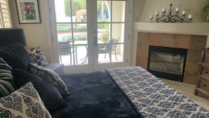 A bedroom with a large bed, a fireplace, and a view of the outdoors through a glass door. - Luxurious Ground floor Villa with 2 Master Bedrms and views (La Quinta)