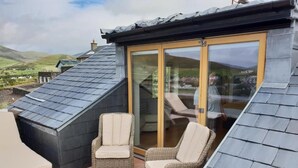 A covered patio with wicker furniture and a glass door leading to a scenic view. - Fab View (Dingle)