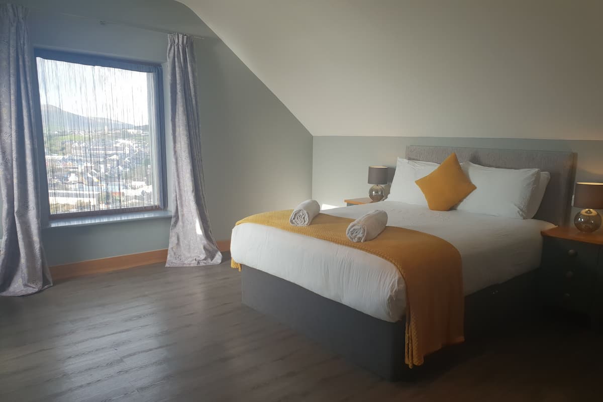 Quarto moderno com uma cama grande, vista para a cidade através de uma janela e piso de madeira.