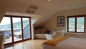 A bedroom with a large bed, a sofa, and a balcony with a view of the countryside. - Fab View (Dingle)
