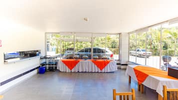Amplio espacio interior con mesas y sillas, una barra de buffet y grandes ventanales con vistas a coches aparcados y zonas verdes.