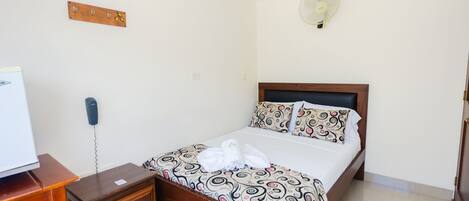 A neatly arranged bedroom with a bed, bedside table, and a wall-mounted fan.