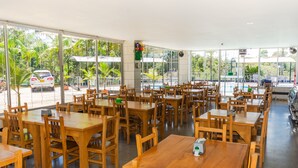 A spacious indoor dining area with wooden tables and chairs, large windows offering a view of the outdoors, and a pool visible through the windows. - Hotel Verony Guatape (Guatapé)