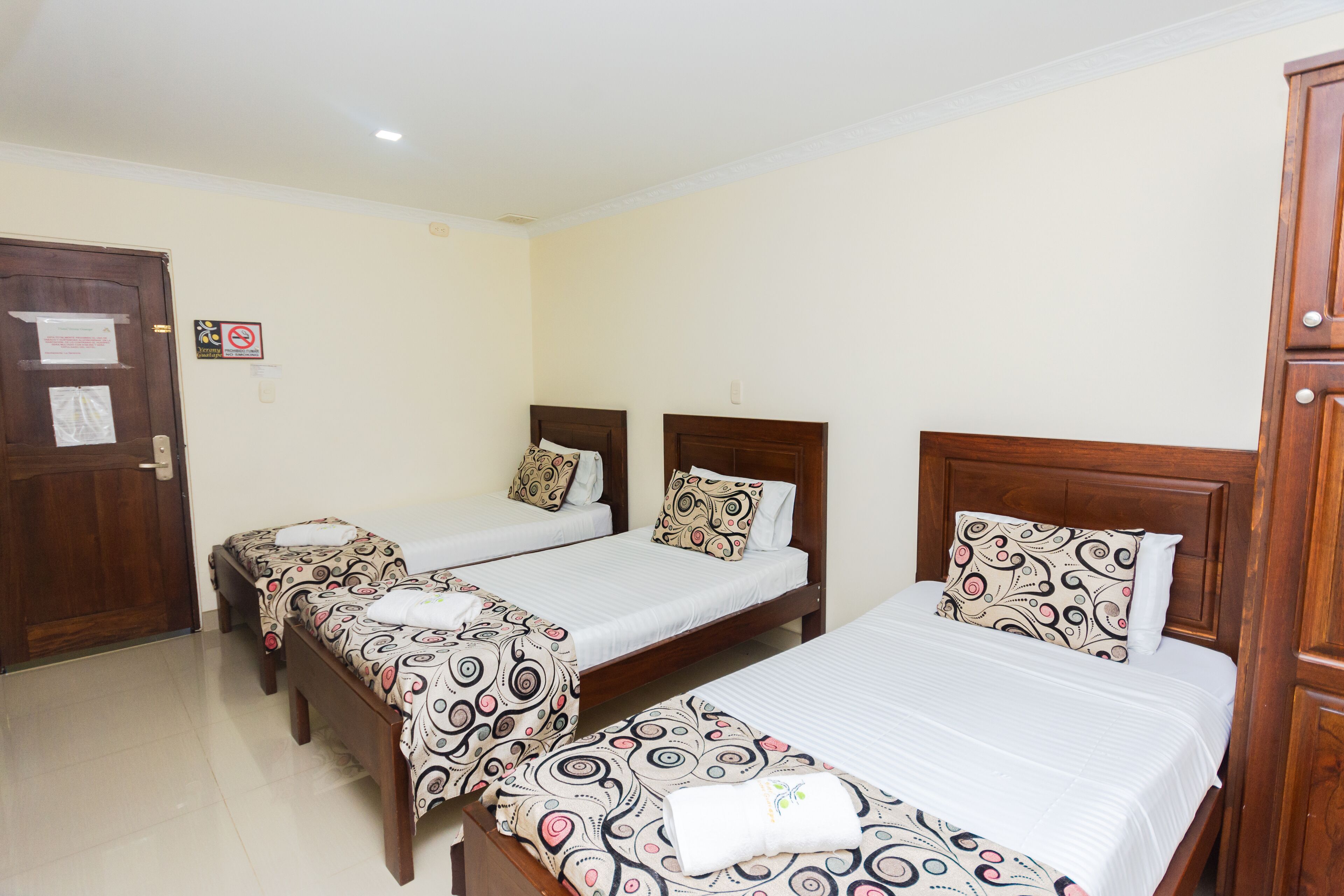 A hotel room with three single beds, each with patterned bedding and wooden headboards.