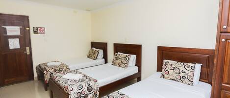 A hotel room with three single beds, each with patterned bedding and wooden headboards.