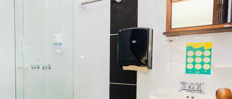 Un baño moderno con cabina de ducha de vidrio, inodoro blanco, lavamanos con espejo y secamanos.