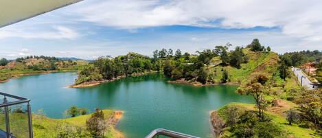 A panoramic view of a lake surrounded by hills and greenery, with a clear sky above.