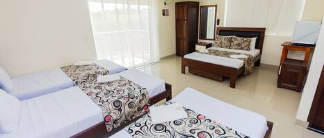 Habitación de hotel con dos camas individuales, una cama doble, un armario, un escritorio con silla y un ventanal con persianas.