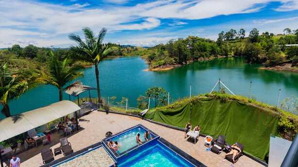 A pool area with a view of a lake, surrounded by greenery and a clear sky. - Hotel Verony Guatape (Guatapé)