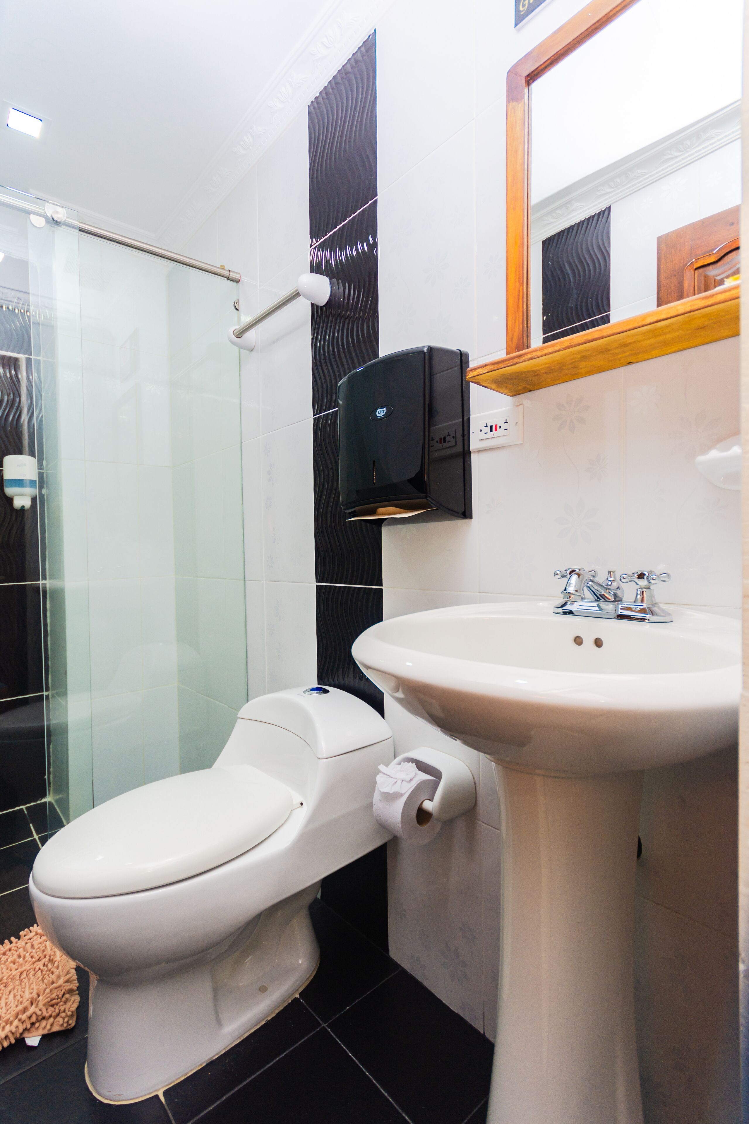 A bathroom with a toilet, sink, and glass shower enclosure.