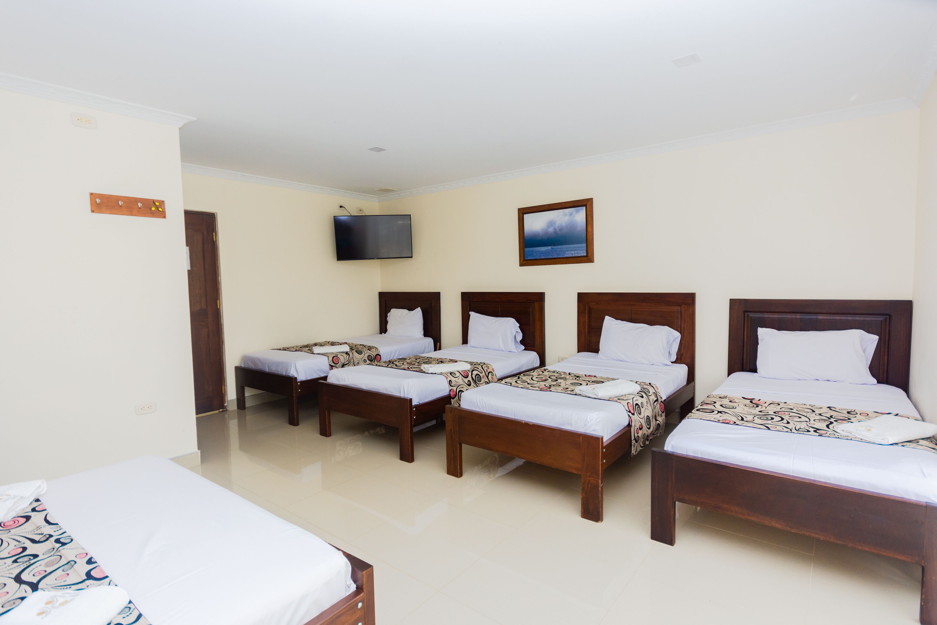 A hotel room with four wooden beds, a television, and a framed picture on the wall.