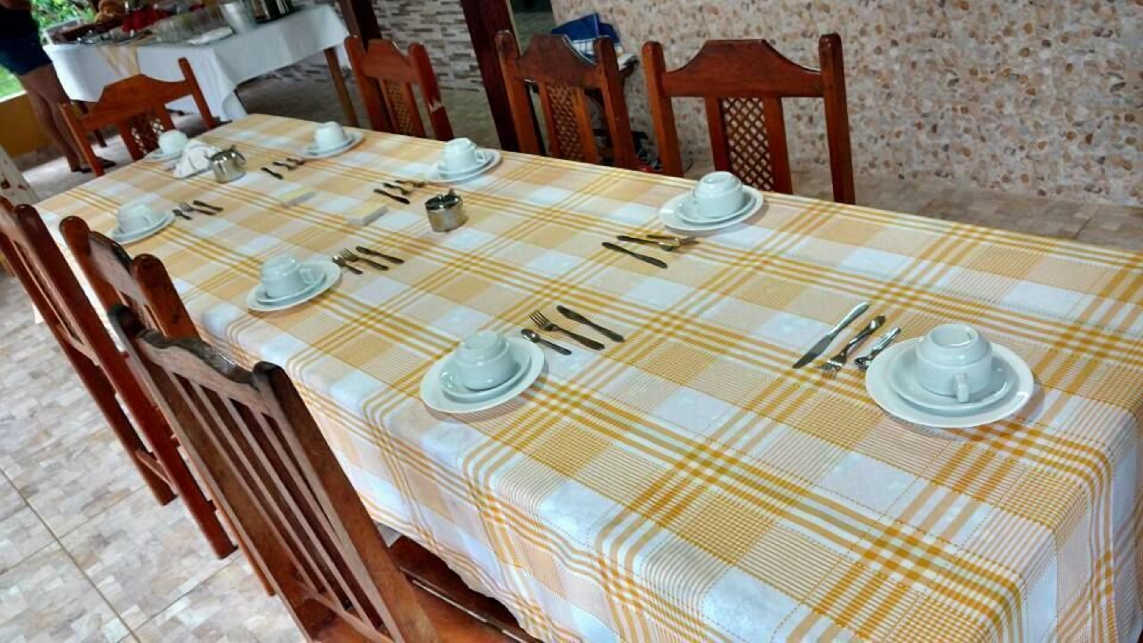 A dining table set with plates, cutlery, and cups, surrounded by wooden chairs.