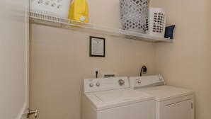 A laundry room with a front-loading washer and dryer, a shelf with laundry baskets, and a framed certificate on the wall. - Super cute and clean studio (Myrtle Beach)