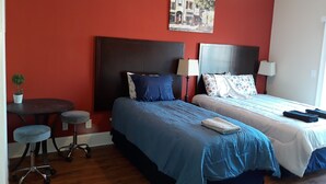 A hotel room with two beds, a small table with a chair, a ceiling fan, and a painting on the wall. - Super cute and clean studio (Myrtle Beach)