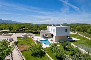 Une maison moderne à deux étages avec une piscine, entourée d’un jardin bien entretenu et dominant un paysage montagneux.