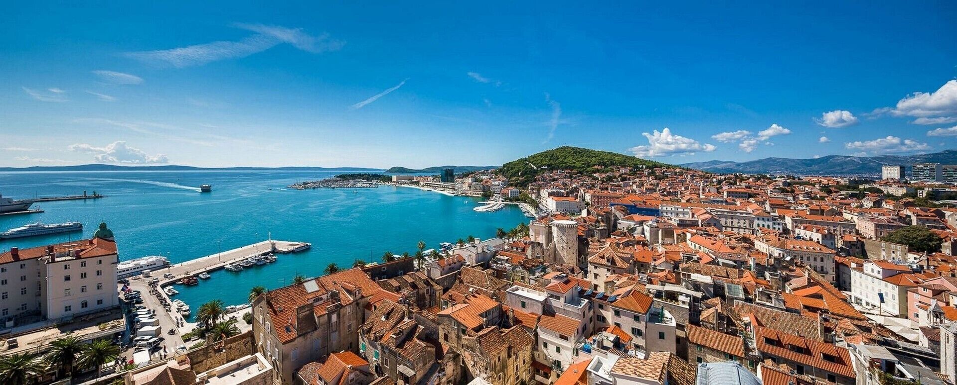 A coastal cityscape with historic buildings, a marina, and a clear blue sea.