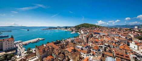 A coastal cityscape with historic buildings, a marina, and a clear blue sea.