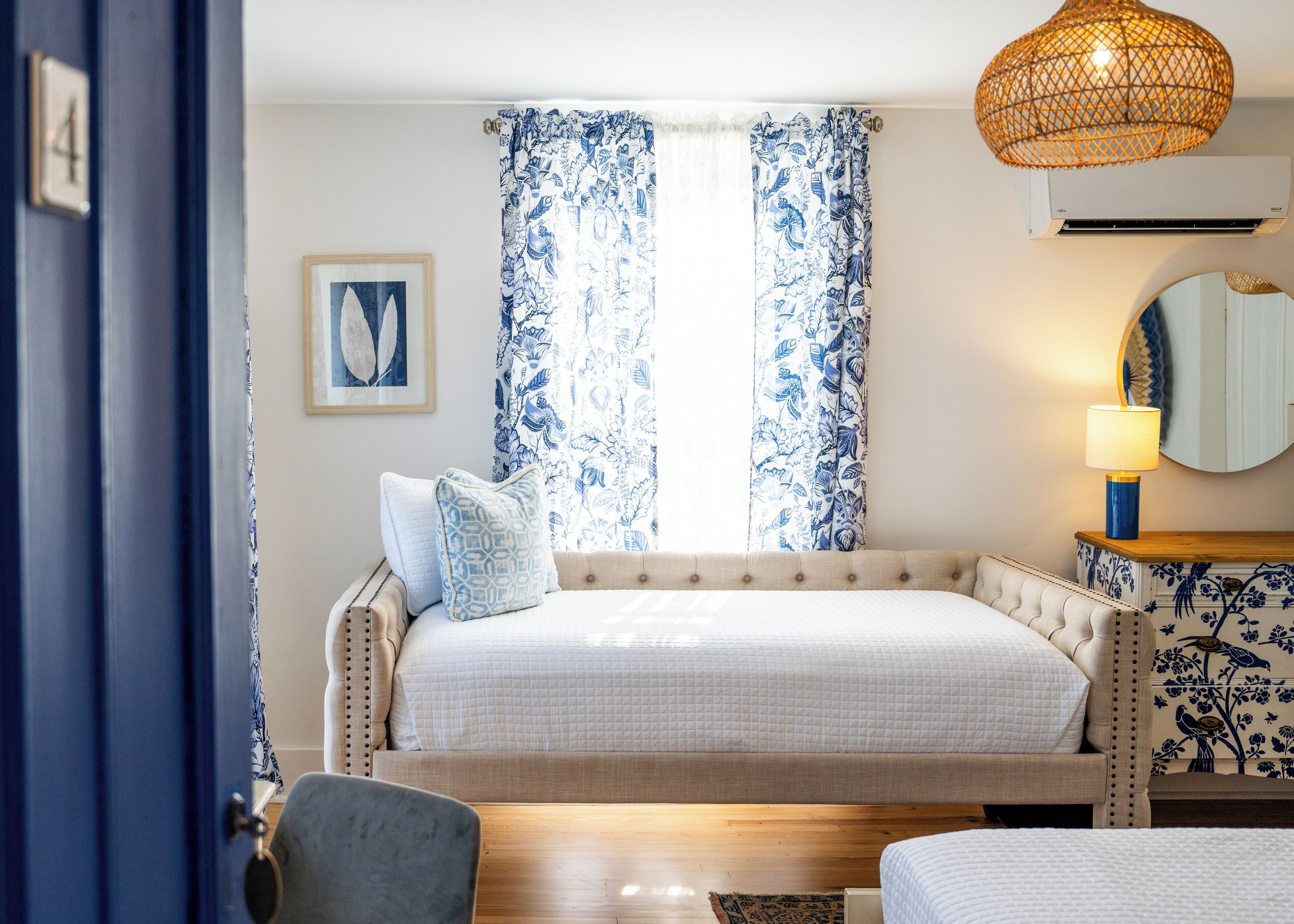 Une chambre à coucher avec un grand lit, des rideaux à motifs floraux, une lampe de chevet, un miroir et une table de chevet en bois.