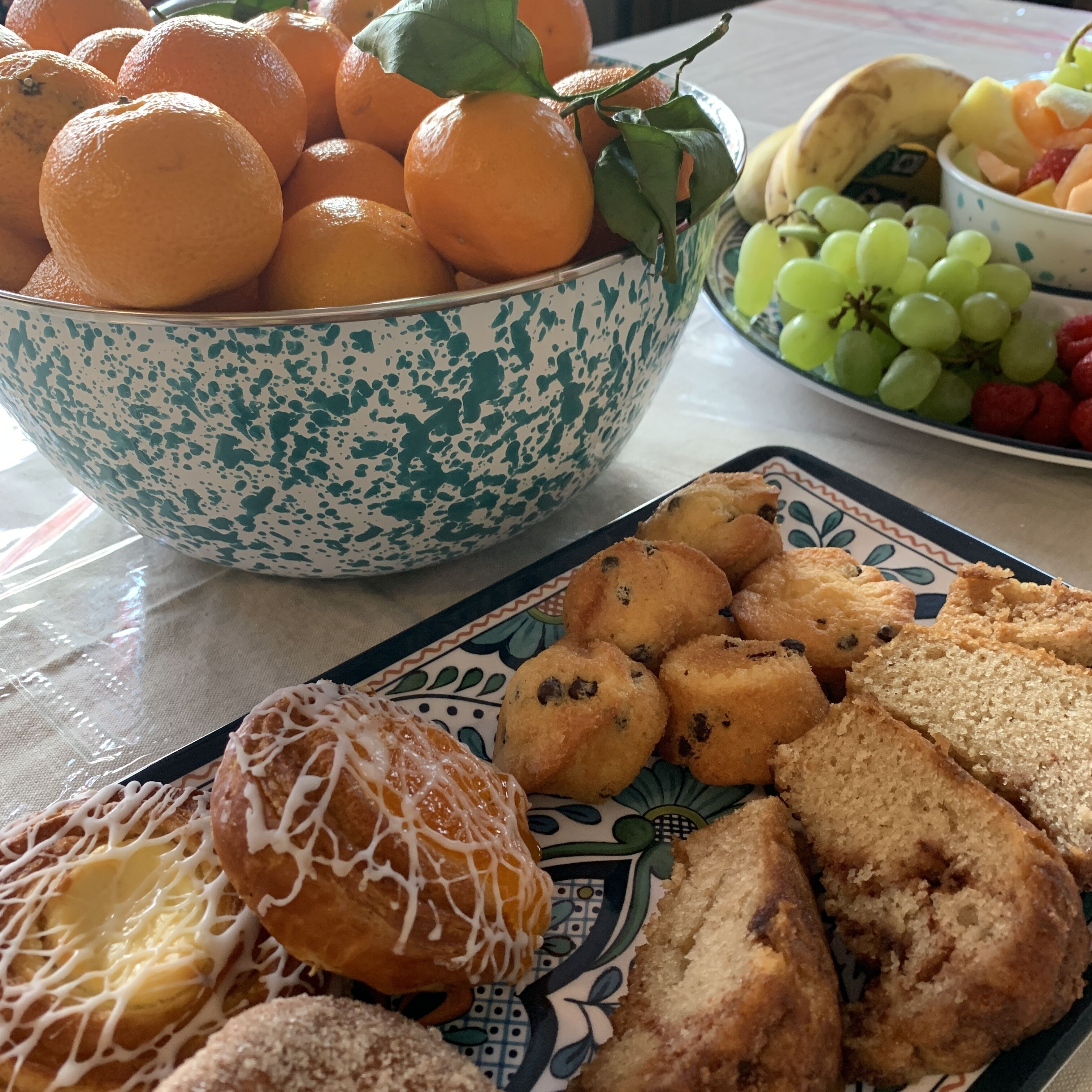 Una mesa con un bol de naranjas, un plato de pasteles y un bol de uvas.