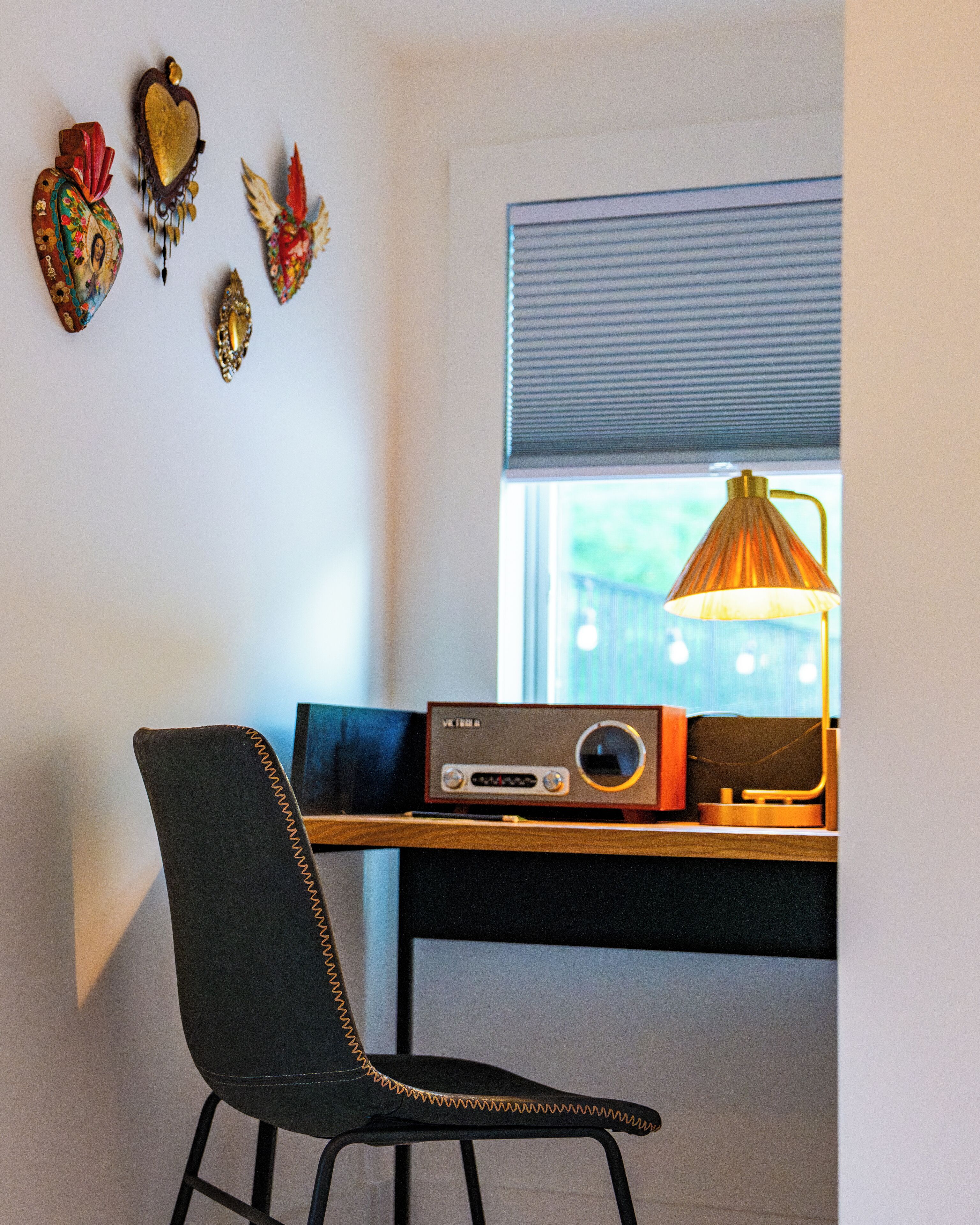 A room with a desk, chair, decorative wall art, and a window with blinds.