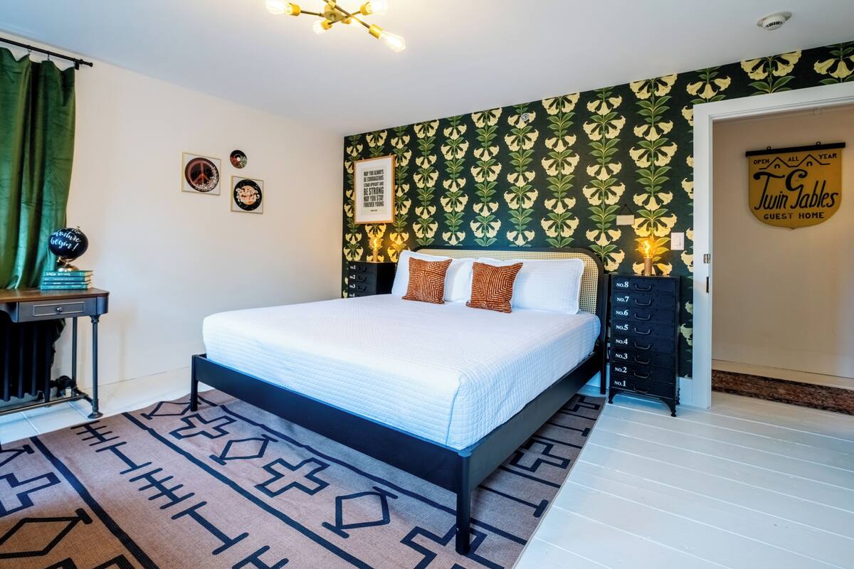Ein Schlafzimmer mit einem Bett, einem Schreibtisch mit Büchern, einer Wand mit floralem Muster und einem Schild an der Wand.