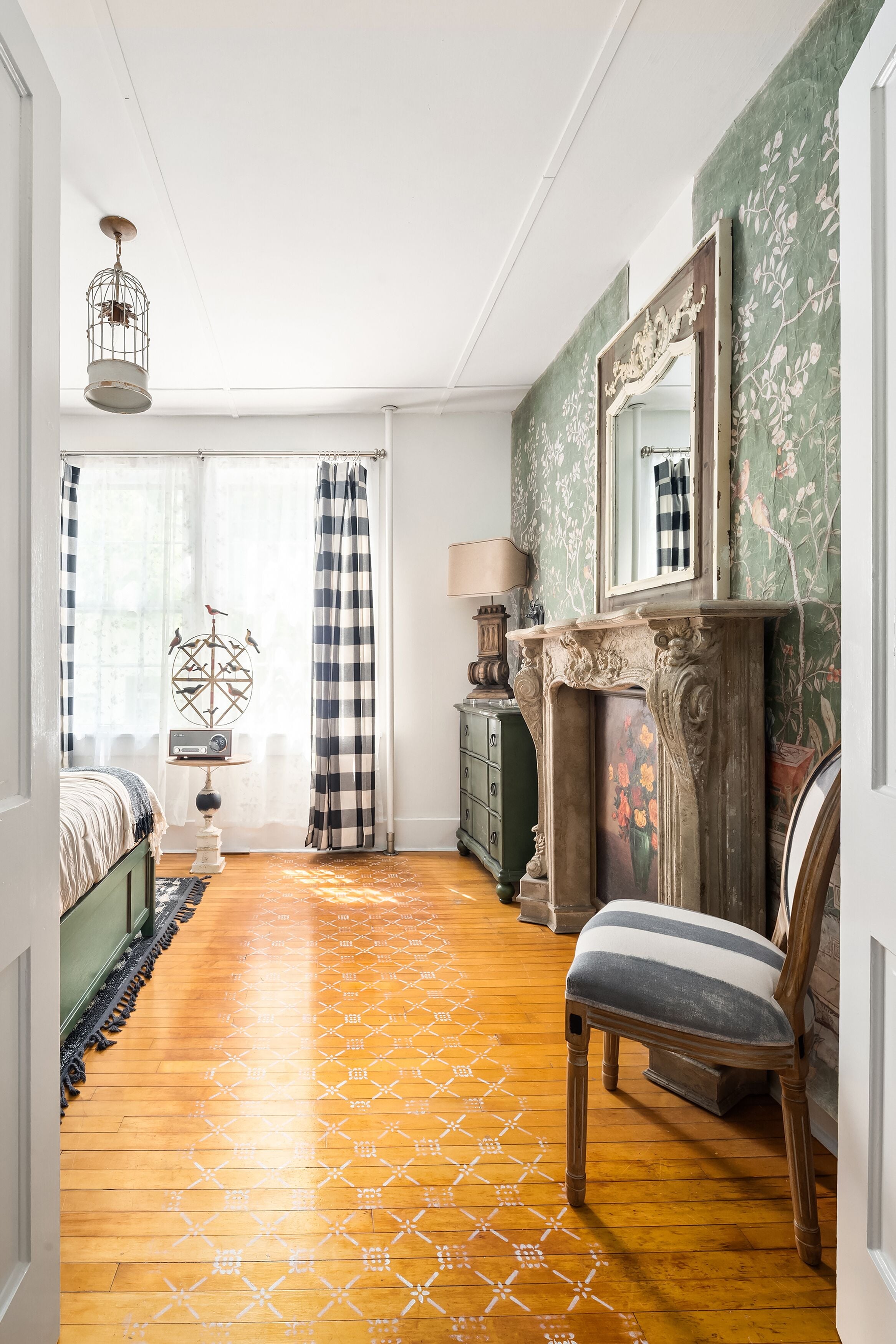 A room with a wooden floor, a bed, a chair, a dresser, a mirror, and a fireplace.
