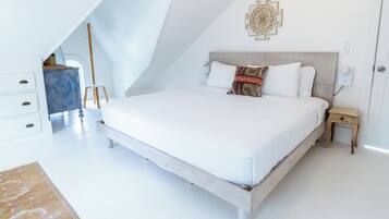 Ein Schlafzimmer mit schräg gedachter Decke, einem Bett mit weißer Bettwäsche, einem Nachttisch aus Holz und einem Wandbild.