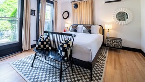 Een moderne slaapkamer met een groot bed, een nachtkastje met een lamp, uitzicht op groen buiten, en een geruit vloerkleed.